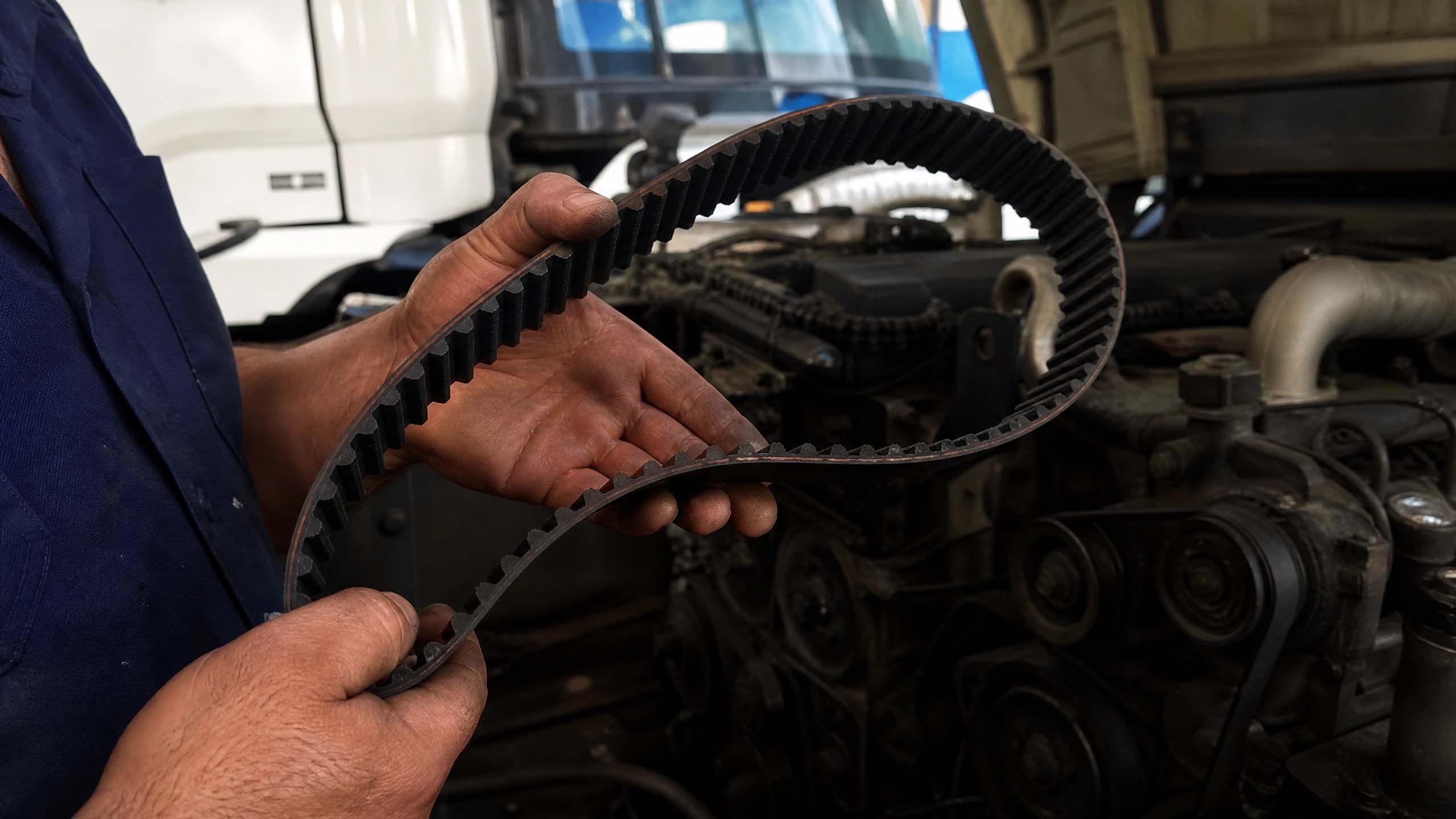 Mecânico segurando correia dentada nova ao lado do motor aberto de um caminhão